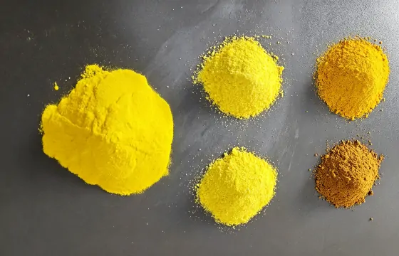 聚合氯化铝粉末散布于灰色平面上，物料呈细小粉状，整体为大小高矮各不相同的不规则土丘状料堆，无固定几何棱角，堆体表面自然凹凸，边缘弥散散落细碎粉料，料堆色泽由亮黄过渡至黄褐色。